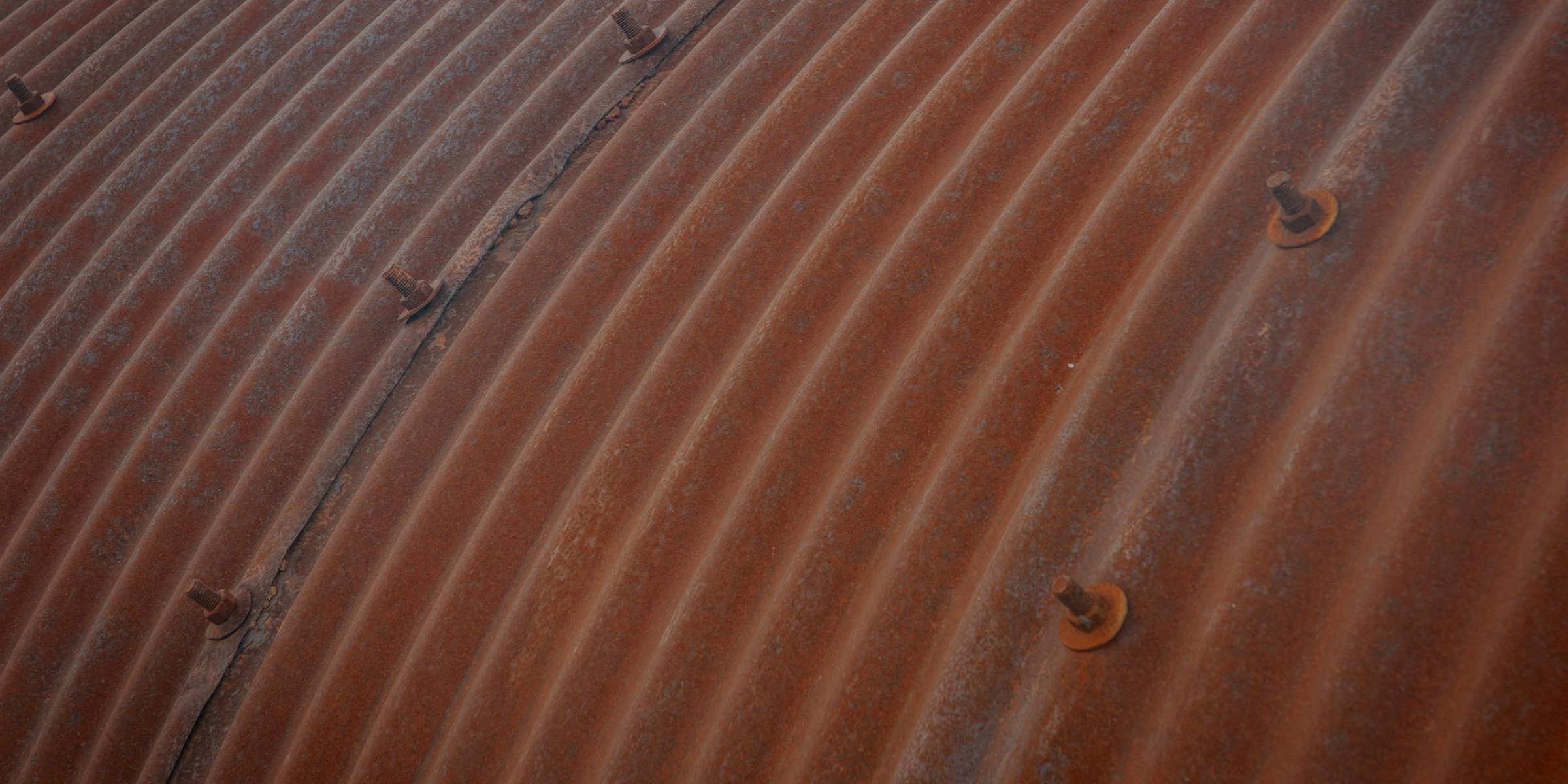 Rusted corrugated steel curving away, bolt heads catching the light