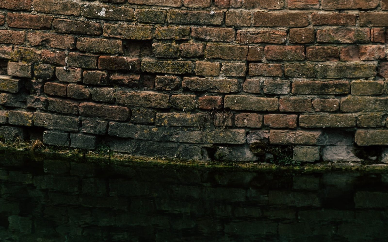 An old brick moat wall meeting dark water, the waterline stained across the stone