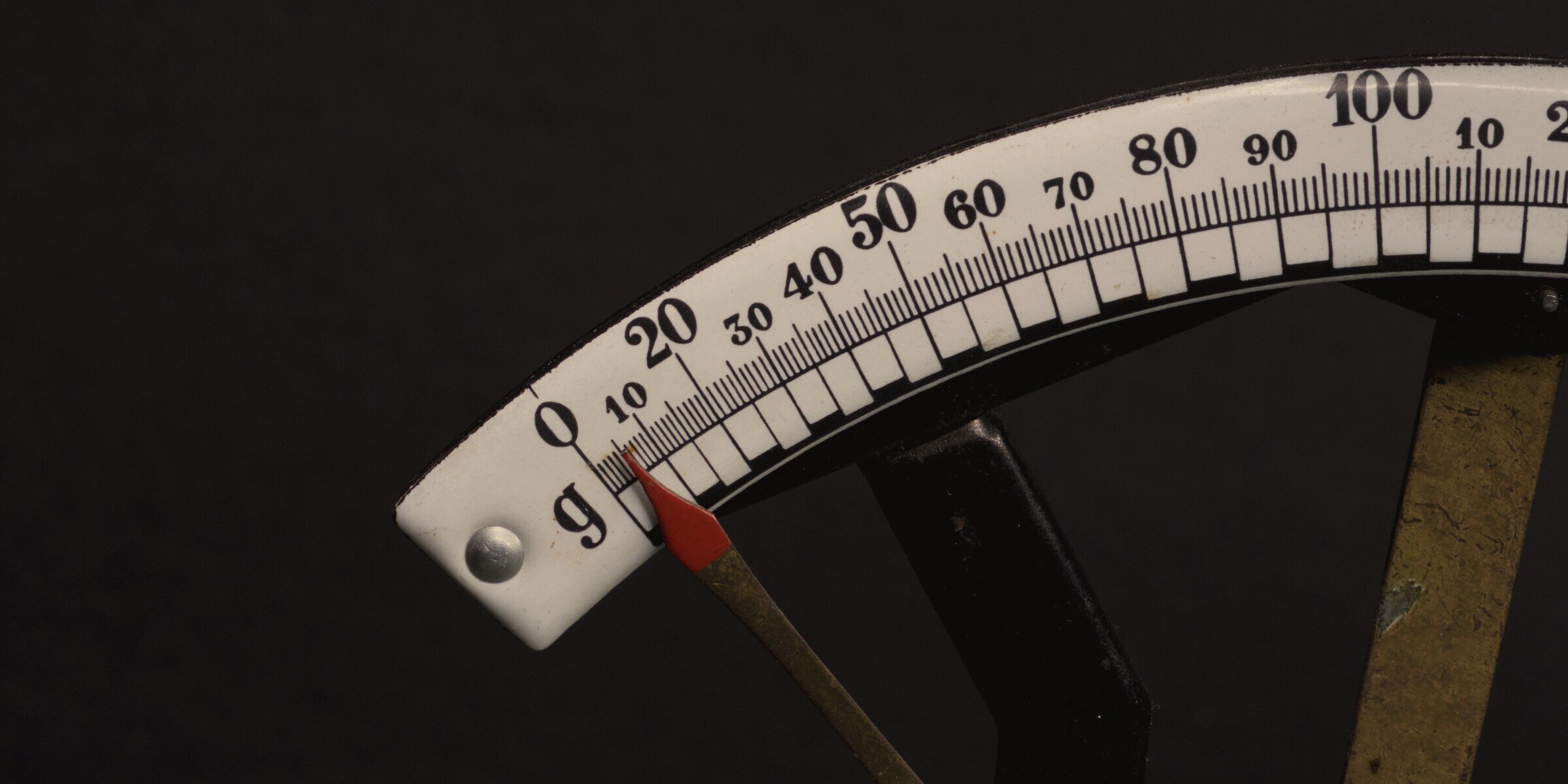 Close-up of a weighing scale dial, its red needle resting at zero